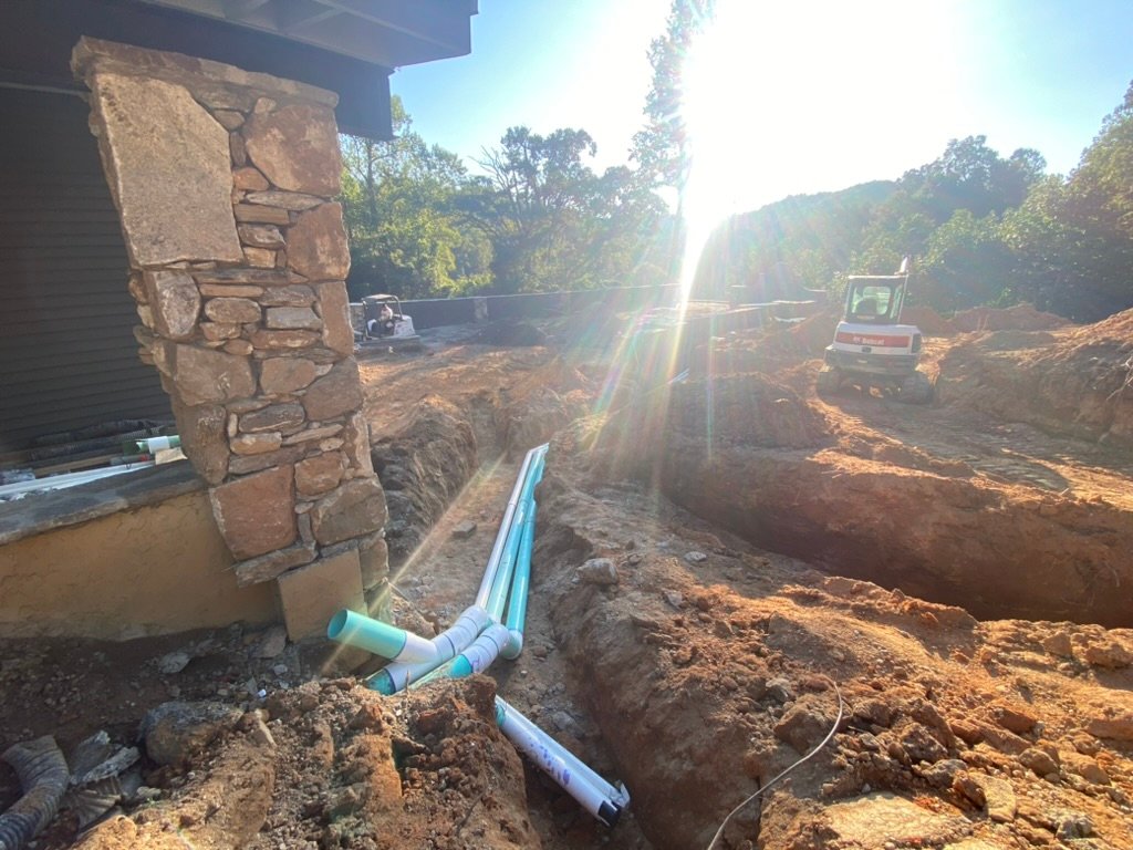 Plumbing rough-in — excavation alongside the stone column with Bobcat on site