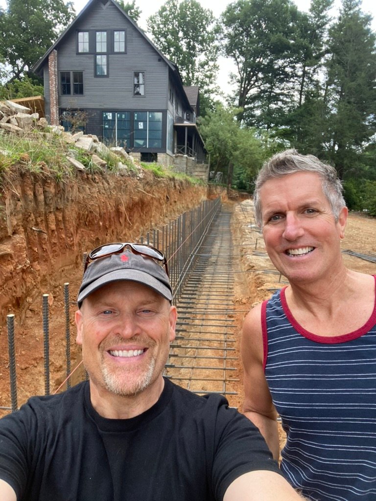 Joel & Jay — selfie on the job site with the inn rising behind them
