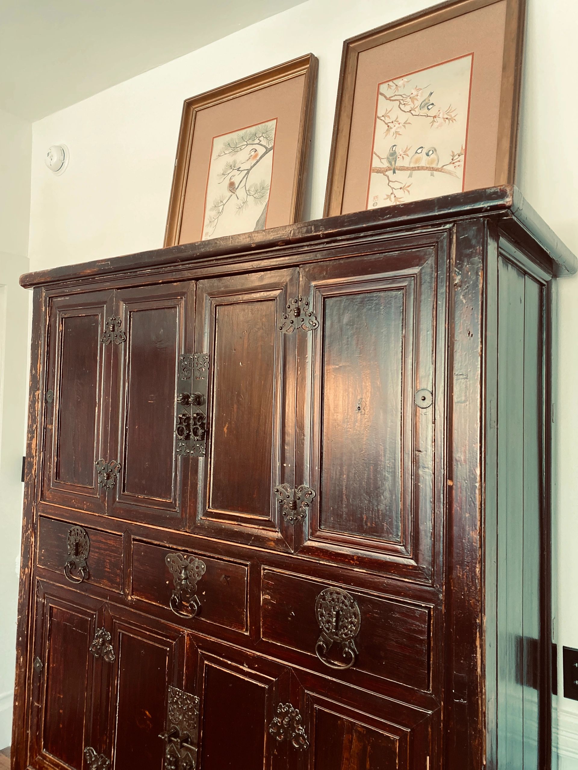 Antique wooden cabinet with ornate metal handles and framed artwork on top